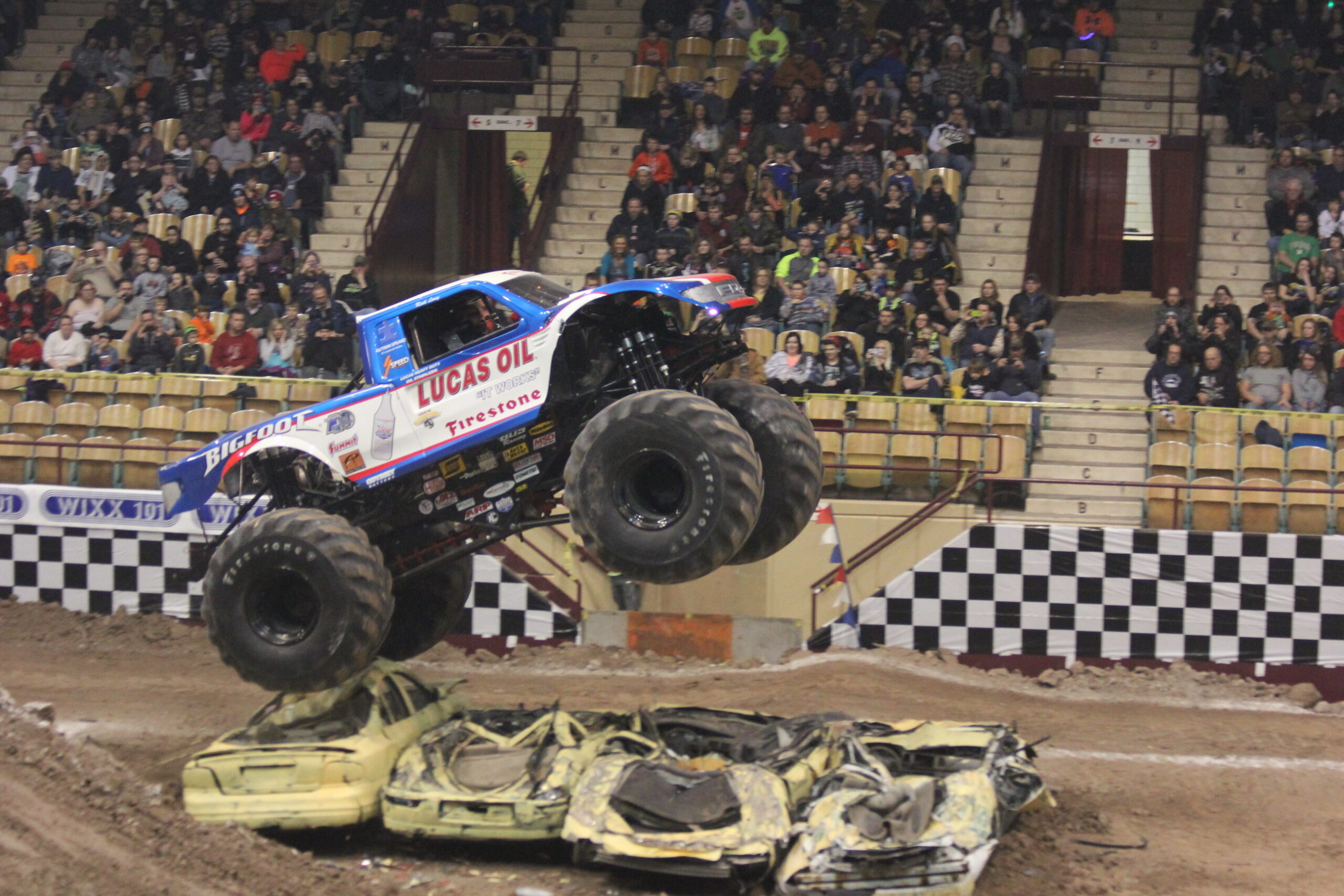 Bigfoot monster truck jumping over crushed cars in packed indoor arena