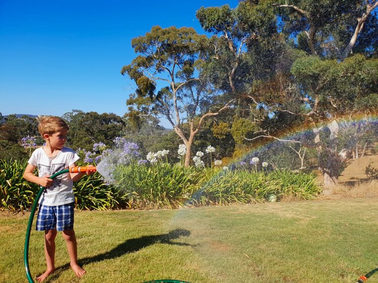 Boy making a rainbow with a garden hose on a summer day