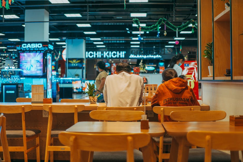 People dining in a vibrant mall food court with colorful lighting and multiple restaurants