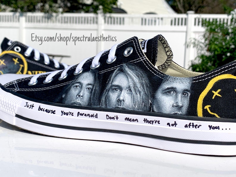 May include: Black canvas Converse sneakers with a custom design featuring the faces of Kurt Cobain, Krist Novoselic, and Dav