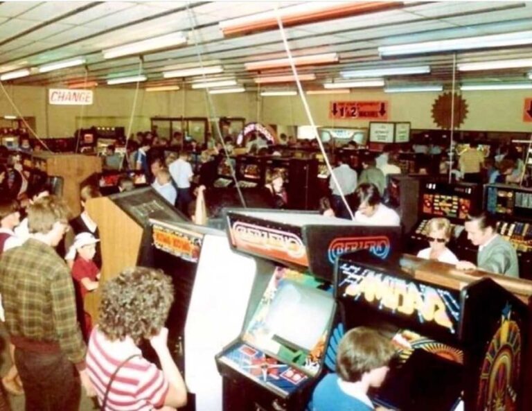 Crowded 1980s video arcade with Pac-Man cabinets and players at the peak of the golden age