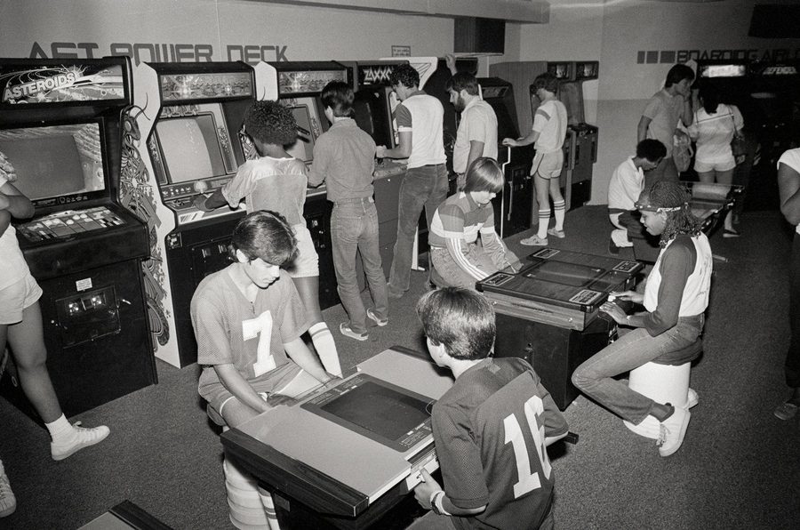 Kids playing Asteroids and Zaxxon arcade cabinets inside an 80s video arcade