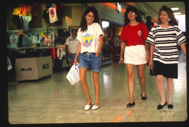 80s mall culture teen shoppers walking through mall corridor with neon signs