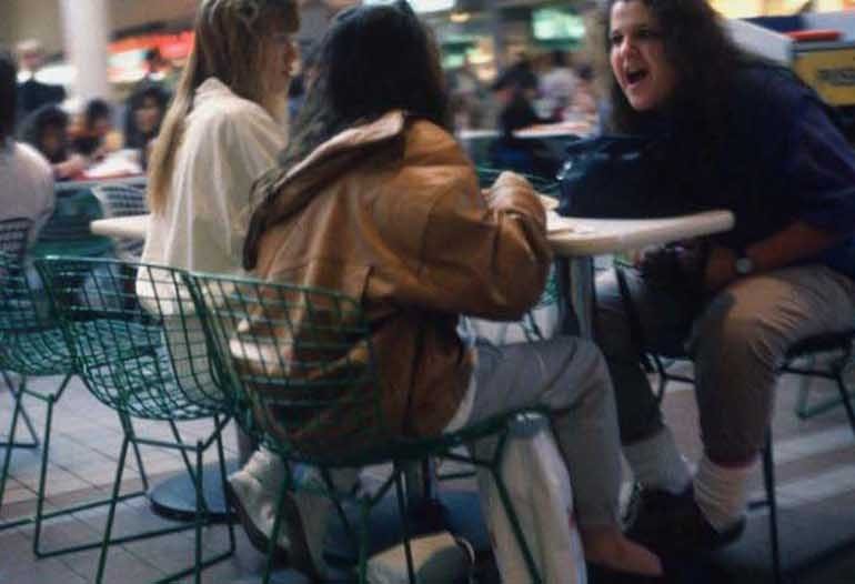 1980s mall food court with teenagers hanging out at green wire mesh tables