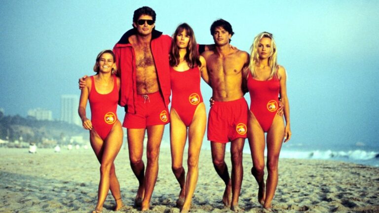 Baywatch cast in red swimsuits walking on the beach