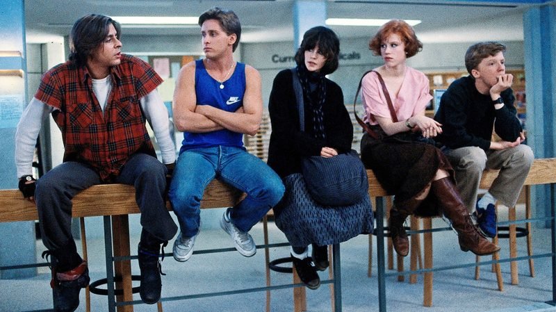 All five Breakfast Club characters sitting on stools in the school library