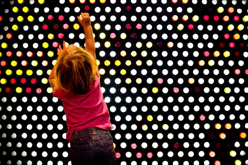 Child placing pegs on a giant illuminated Lite-Brite light wall