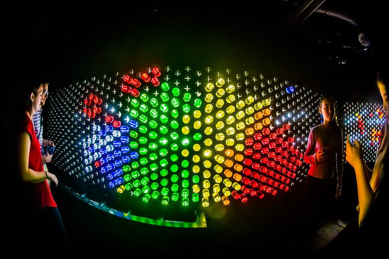 Giant Lite-Brite peg wall installation glowing in rainbow colors