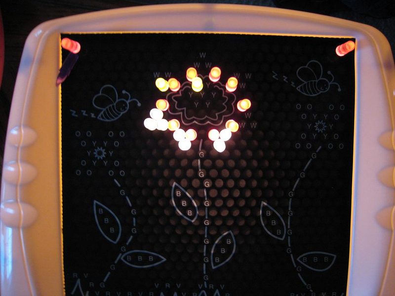Lite-Brite screen showing a flower template glowing with yellow and white pegs