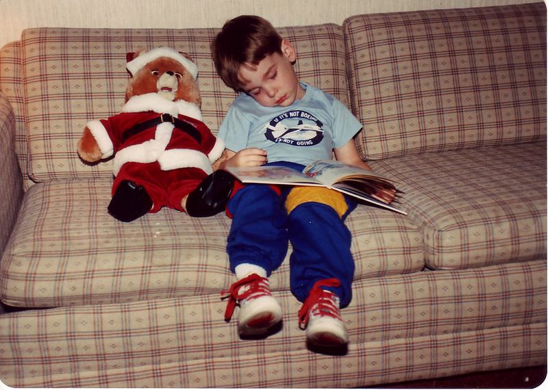 Teddy Ruxpin in a Santa outfit beside a boy reading the storybook