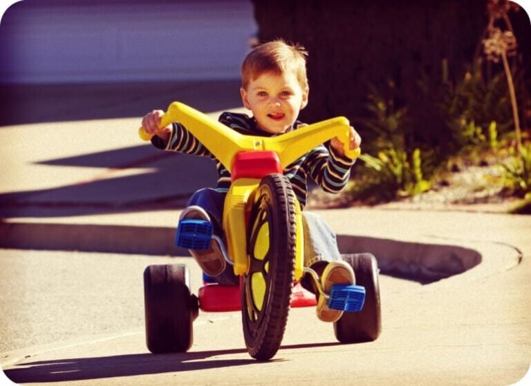 Boy riding a classic yellow and red Big Wheel toy tricycle in the 1970s