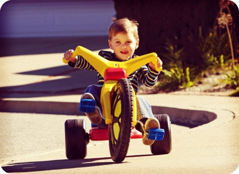 Boy riding a classic yellow and red Big Wheel toy tricycle in the 1970s