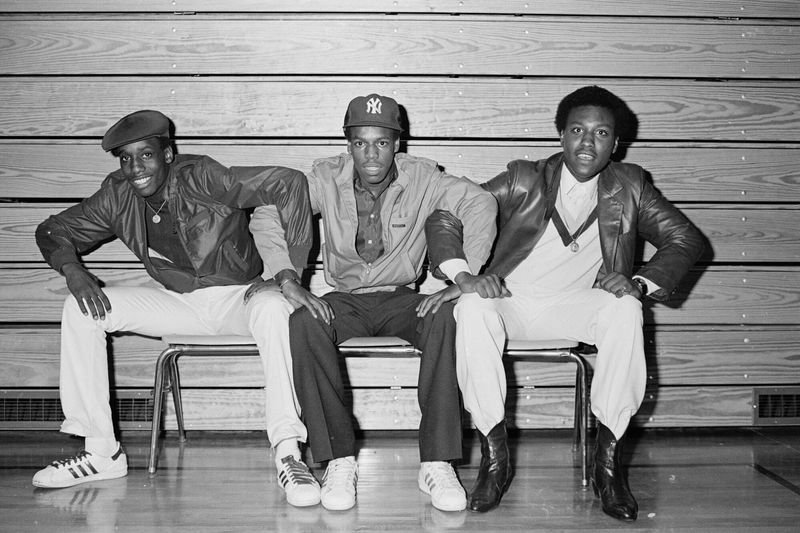 Three young Bronx men in early hip-hop fashion - Adidas, leather jackets, NY cap