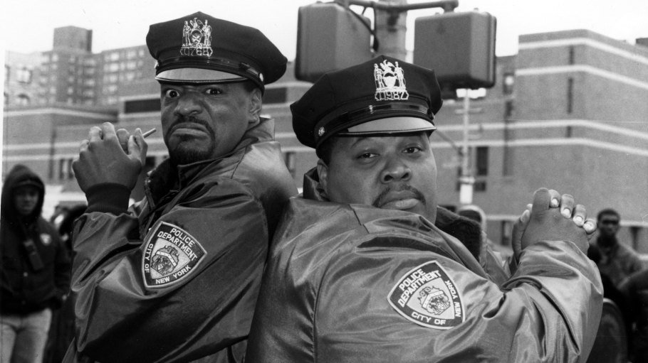 Ed Lover and Doctor Dré dressed as New York City Cops, are back-to-back holding imaginary guns.