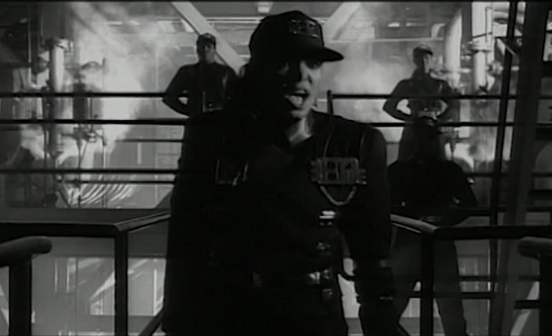 Janet Jackson in military uniform and cap singing in the Rhythm Nation music video