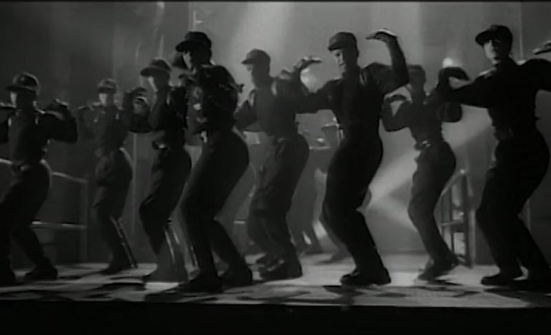 Rhythm Nation dancers in unisex military uniforms performing the iconic choreography line