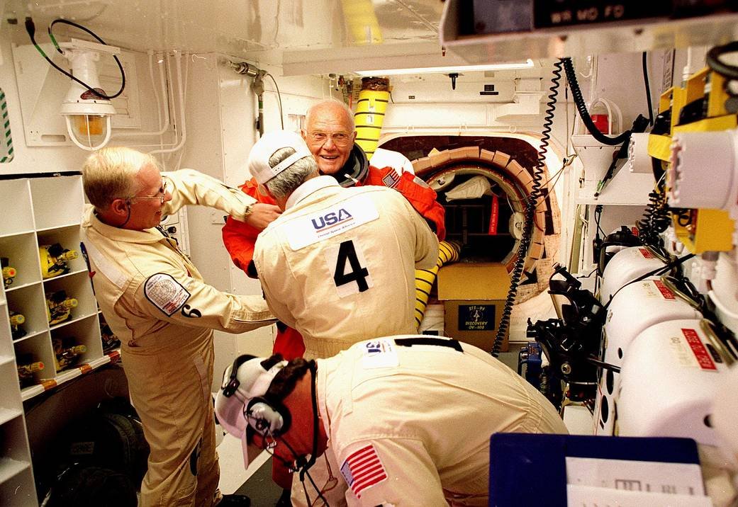 Senator John Glenn smiling in the White Room as closeout crew check his flight suit before boarding Space Shuttle Discovery on October 29, 1998