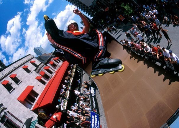 Aggressive inline skater performing a vert ramp trick in front of a crowd